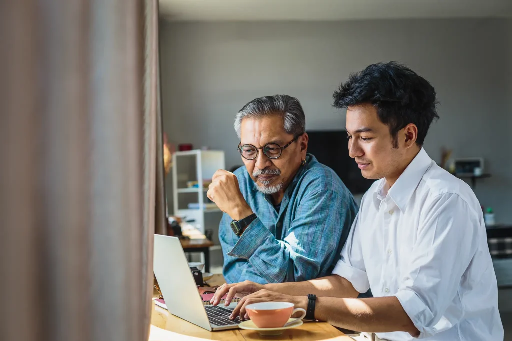 younger man helping older man on laptop