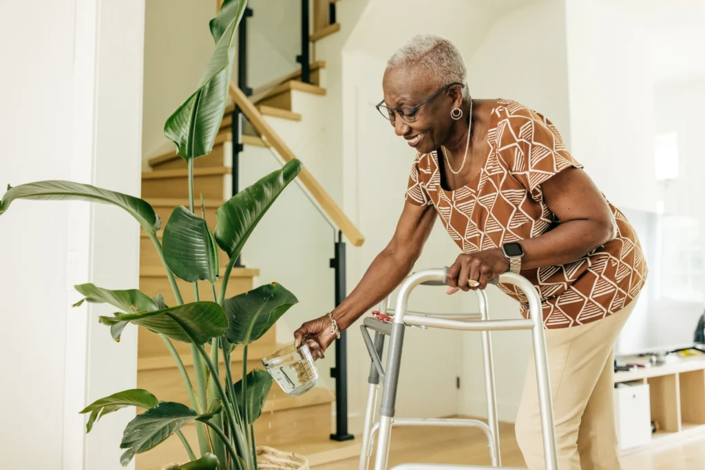 elderly woman watering plant while using walker